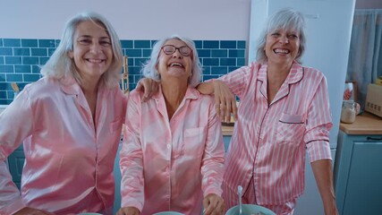 Wall Mural - Senior women in pink colored pajamas making a pajama party at home. Making breakfast in the morning and having fun. Concept about seniority and staying young.