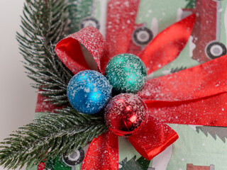 A beautifully wrapped Christmas present features vibrant red ribbons, winter-themed paper, and colorful ornaments. Pine branches and snow add to the festive atmosphere, embodying holiday spirit.