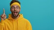 © Jenny - Excited young caucasian male in yellow hoodie pointing up with expression against blue background