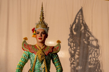 Wall Mural - One man with Khon or Mask dance dress stand with performance action in front of grand shadow play in the background with white screen.