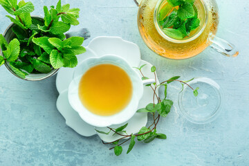 Poster - Mint tea. A cup of peppermint tea with fresh mint leaves and a tea pot, overhead flat lay shot on a blue background