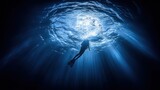 Silhouette of scuba diver swimming underwater, sunlight beams through the water surface.