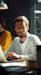 Poster - Young man working intently at a laptop in a modern, minimalist workspace during a sunny afternoon