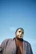 © Studio Sincère/Stocksy - Masked figure in gold beneath clear skies