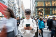 © Alvaro Lavin/Stocksy - Smiling woman using smartphone on busy manhattan street, new york city
