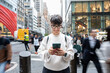 © Alvaro Lavin/Stocksy - Smiling tourist using smartphone in busy manhattan street