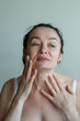 © Olena Smyrnova/Stocksy - Portrait of mature woman applying cream on her face and neck