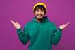 © ViDi Studio - Young shocked surprised impressed fun happy Indian man he wears green hoody yellow hat casual clothes spread hands look camera isolated on plain purple background studio portrait. Lifestyle concept.