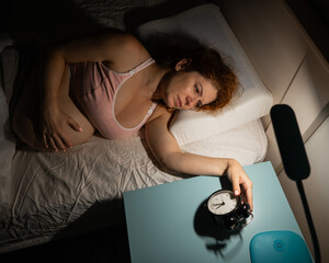 A pregnant woman lies in bed and holds an alarm clock. 