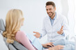 © Prostock-studio - Friendly dentist handsome millennial man in workwear having conversation with blonde woman patient sitting at dental chair, smiling and gesturing, side view. Doctor and patient relationship