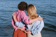 © Nika Oksenchuk/Stocksy - Two women stand on the beach beside the ocean, enjoying a sunny day