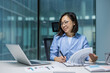 © Liubomir - Joyful and successful Asian woman doing paperwork inside the office, businesswoman financier preparing reports and contracts, filling out economic indicators and tax forms, using laptop.