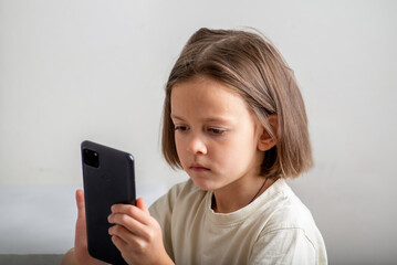 Little child uses the phone on a light background with copyspace