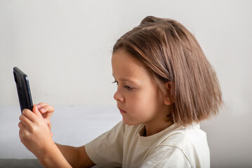 Little child uses the phone on a light background with copyspace