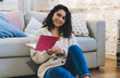 © BullRun - Smiling woman sitting on floor with notebook