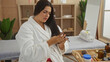 © Krakenimages.com - Woman wearing a white robe examining her hair in a spa room with a massage table and beauty products in the background