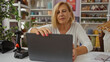 © Krakenimages.com - Mature blonde woman using laptop in home decor store with shelves in background and scanner on counter