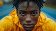 © Enggal Pitoyo - Close-up portrait of a sweaty young Black man with dreadlocks, wearing a yellow raincoat, looking intensely at the camera.