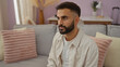 © Krakenimages.com - Young hispanic man with beard sitting in cozy living room at home with pastel decor and soft pillows