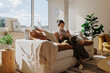 © BONNINSTUDIO/Stocksy - Woman reading a magazine on a comfortable sofa in a sunny living room