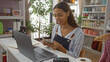 © Krakenimages.com - Young woman working in a home decor store counting money at a desk with a laptop and various decorations on shelves in the background.