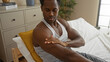 © Krakenimages.com - Young man applying cream to his arm while sitting on a bed in a cozy bedroom at home.