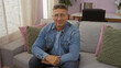 © Krakenimages.com - Man with glasses sitting on a couch indoors in a cozy living room, showcasing a casual and relaxed atmosphere with pillows and a desk in the background.