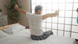 © Krakenimages.com - Middle-aged man stretching on bed in cozy bedroom with white bedding and greenery near window