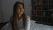 © Krakenimages.com - Woman sitting on bed in a bedroom with thoughtful expression, brunette hair, wearing white shirt, indoors with bedroom furniture, suggesting deep contemplation.