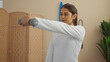 © Krakenimages.com - Woman exercising indoors with dumbbell in a gym setting with a wooden room divider and plant in the background.