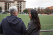 © Lupe Rodriguez/Stocksy - Senior father with adult daughter watching soccer game outdoors