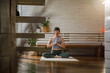 © Jovo Jovanovic/Stocksy - Active young female meditating in living room at home