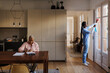 © BONNINSTUDIO/Stocksy - Caregiver cleaning windows while senior woman sitting on dining table