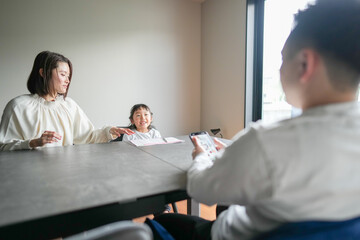 Wall Mural - A Japanese parent and child, a woman in her 30s, a man in his 20s, and a 6-year-old girl, are studying at a table in their living room.