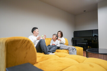 A Japanese parent and child, a woman in her 30s, a man in his 20s, and a 6-year-old girl, are relaxing on a sofa in their living room.