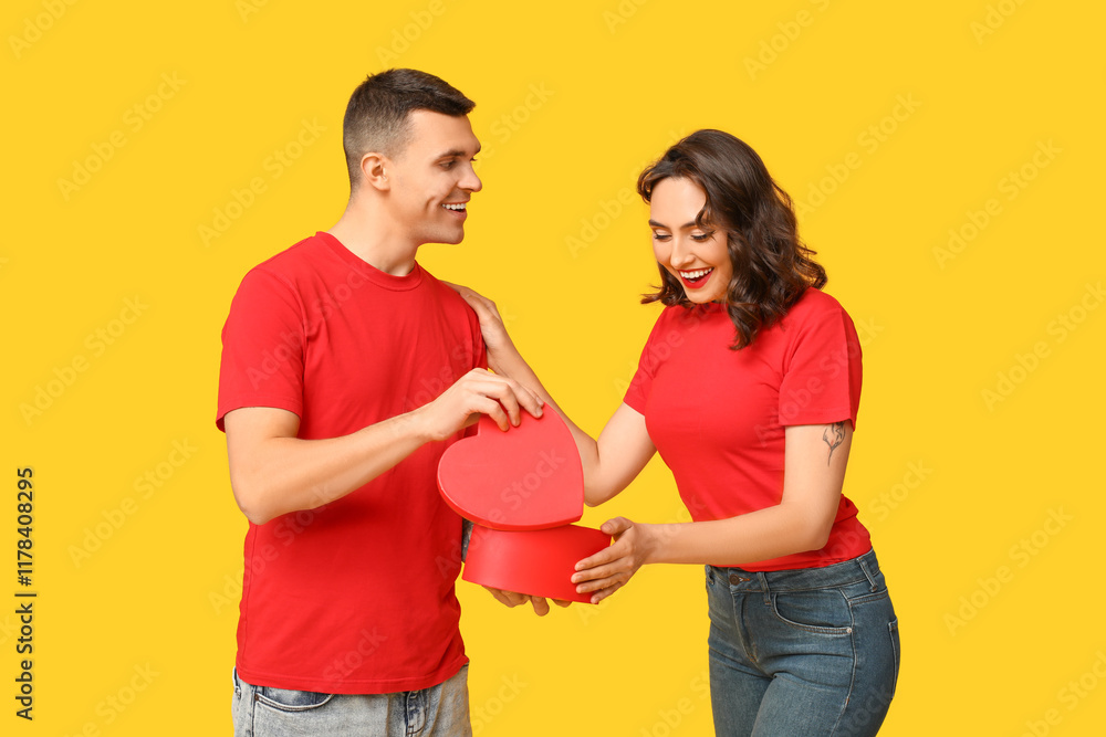 Loving young couple with gift box on yellow background. Celebration of Saint Valentine's Day