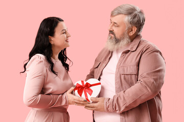 Wall Mural - Beautiful mature couple with gift box on pink background. Valentine's Day celebration