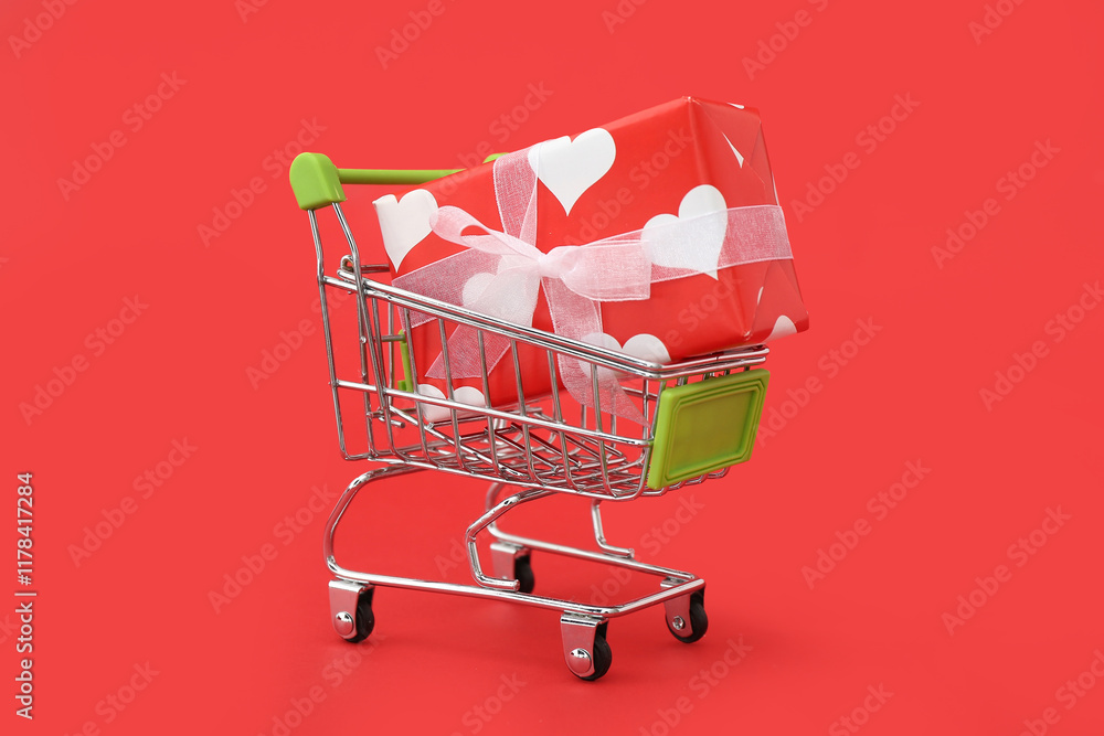 Small shopping cart with gift box on red background. Valentine's Day celebration