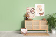 © Pixel-Shot - Chest of drawers, pictures and houseplant near green wall in room