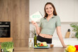 © Pixel-Shot - Sporty young woman holding notebook with word KETO and healthy food on table in kitchen