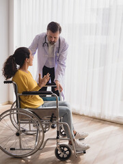 Health care latin woman sick sit wheelchair with man doctor caucasian two people check and treat patients talk help support explain medicine sick person in take care your health hospital clinic room.