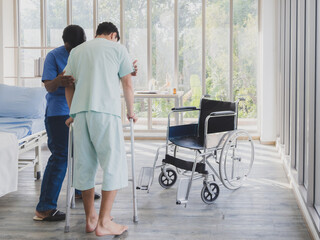 Wall Mural - Patient caucasian man stand crutches walker with woman nurse black people carer physical therapist two person stand talk helping support give advice feel relax smile happy in room clinic hospital.