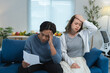 © crizzystudio - Young asian couple sitting on a sofa in their living room, looking worried while reading a letter together, expressing concern and stress over financial troubles and bad news