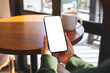 © Farknot Architect - Mockup image of a woman holding mobile phone with blank desktop screen in cafe