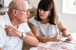 © luciano - Senior couple sitting at home table with paper documents. Elderly man and woman reading documents, paying bills, managing bank finances, calculating taxes, planning loan, debt, insurance, pension