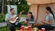 © Summit Art Creations - Family together camping. Mother and daughter listening father play guitar. Parent use outdoor camping activity to communicate and spending time with young generation cross generation gap. Divergence.