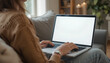 © bellolabs - A woman sitting on a couch, working on a laptop. The laptop screen is blank, and the setting is cozy with soft lighting and plants in the background.