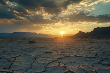 Wall Mural - sun setting over a barren desert landscape. the cracked earth in the foreground illustrates the hars