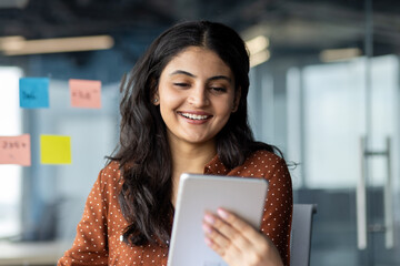 Wall Mural - Businesswoman using tablet computer at work inside office. Smiling woman using app and reading electronic report.