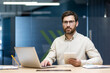 © Tetiana - Portrait of a young serious businessman sitting in the office at the desk, holding a tablet in his hands and confidently looking at the camera